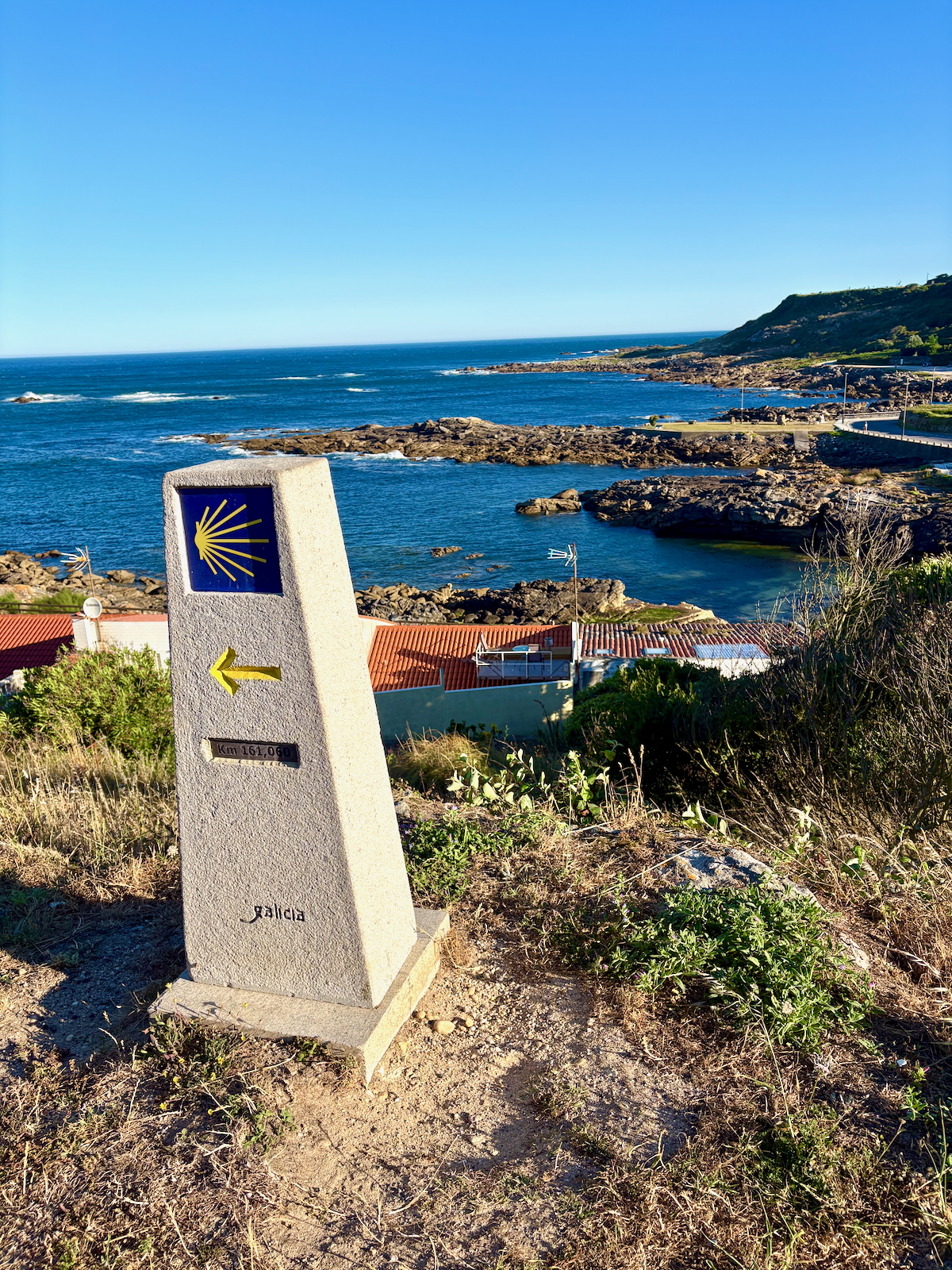 Camino de Santiago milestone at the coast with a yellow shell symbol and a left-pointing arrow in Galicia