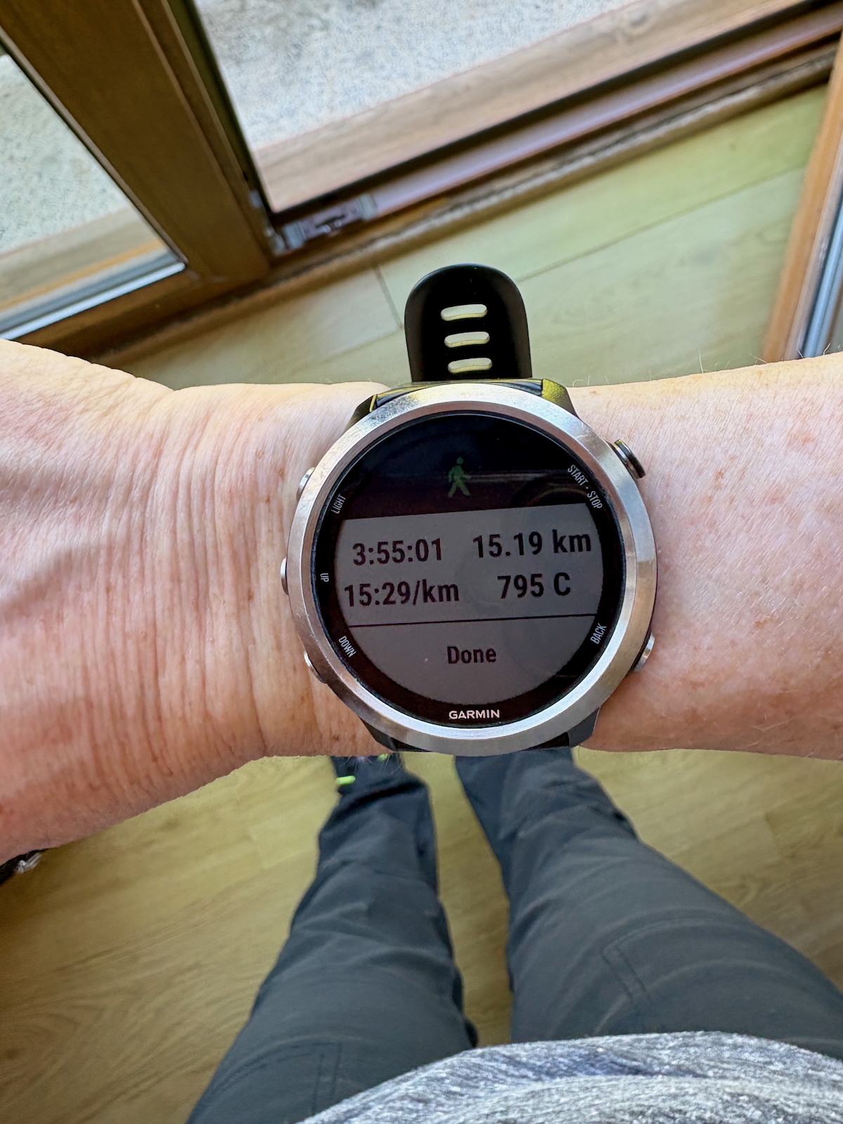 Garmin smartwatch on the wrist showing running stats: 15.19 km, time 3:55:01, pace 15:29/km, calories 795, Done.