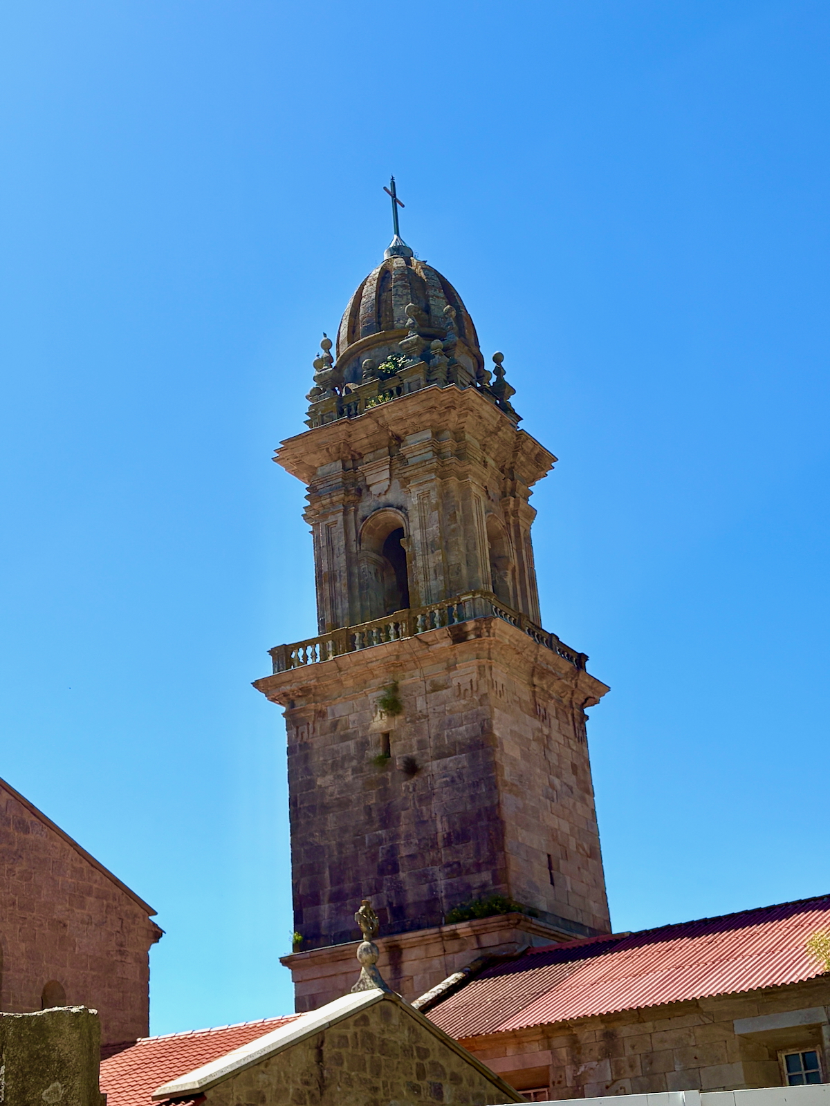 Stone medieval church tower with a dome and cross, set against a bright blue sky.