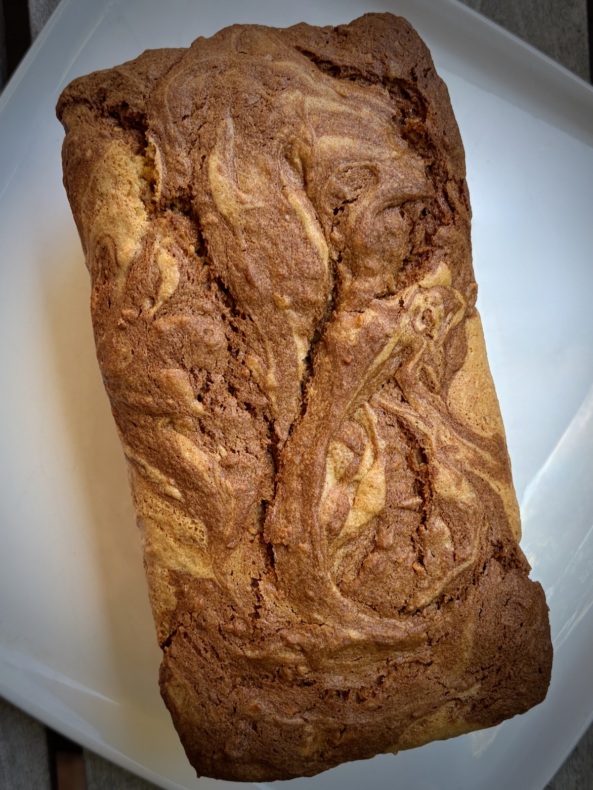 Brown loaf of banana bread with a cracked, swirled top resting in a white baking dish.