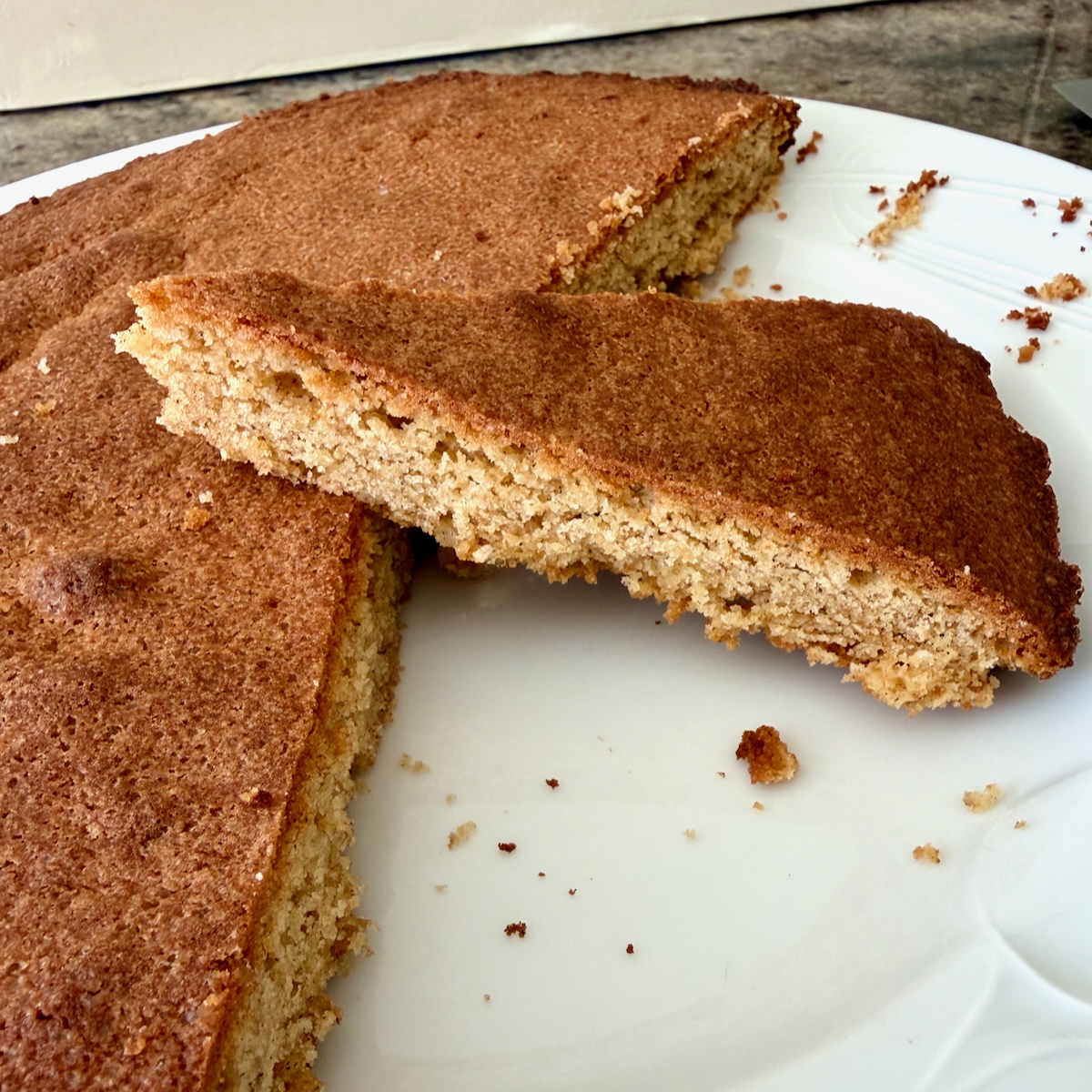 Sliced Breton Buckwheat Butter Cake with a golden brown crust on a white plate, crumbs scattered nearby.