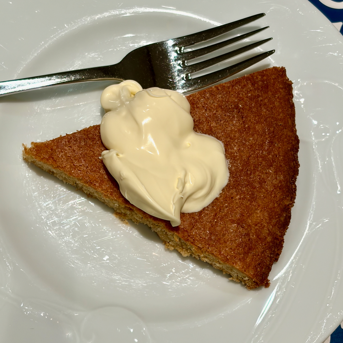 Triangle slice of Breton Buckwheat Butter Cake on a white plate with a dollop of cream and a fork nearby.