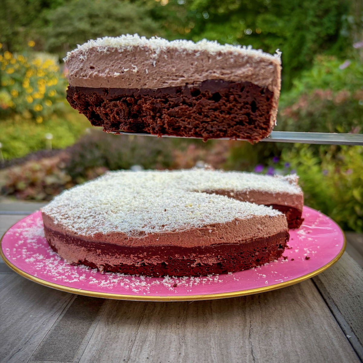 A slice of Dorie Greenspan's Lisbon Cake on a pink plate with a garden in the background.